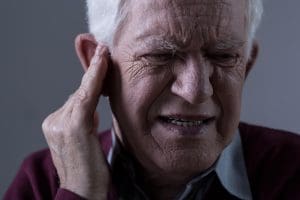 Elderly man holding ear in agony